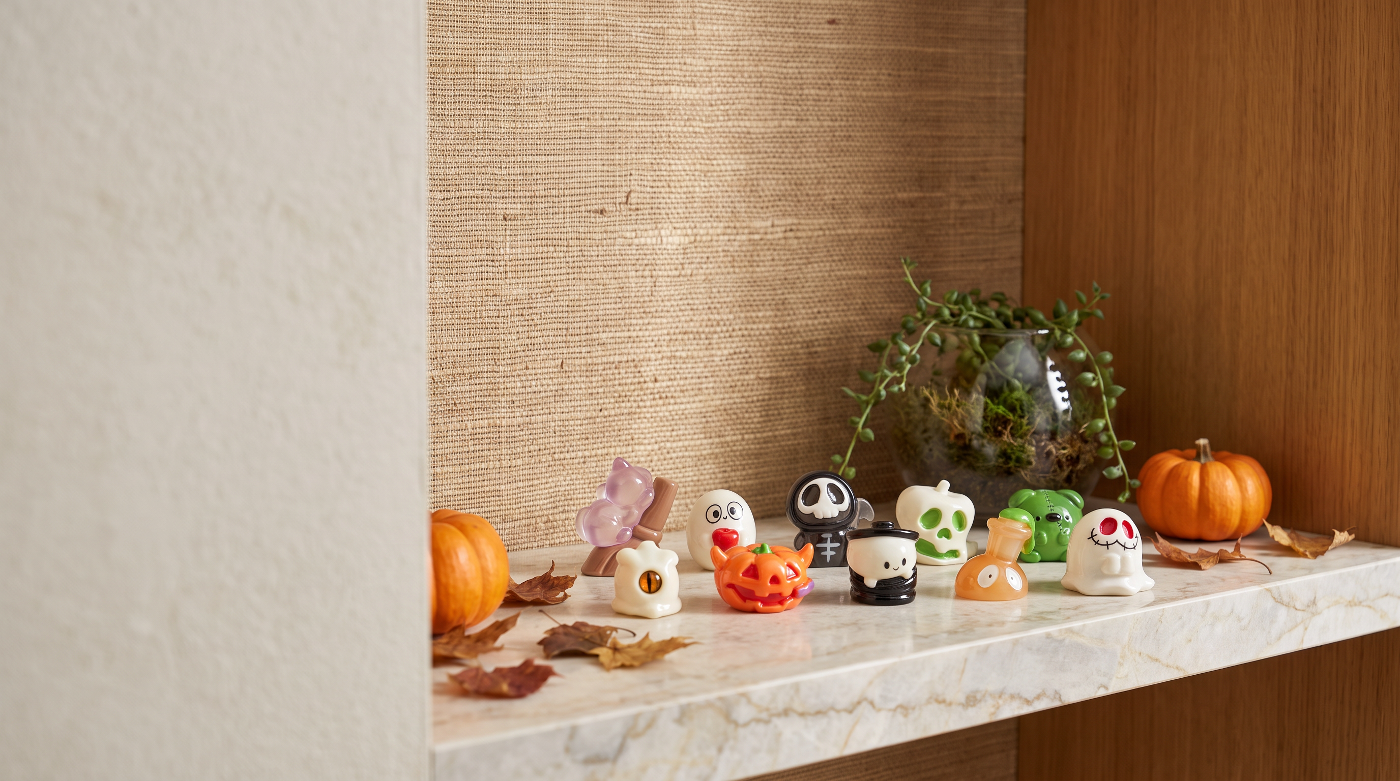 Glow-in-the-dark Halloween miniature figurines styled among moss and mini pumpkins next to a terrarium, warm autumn interior